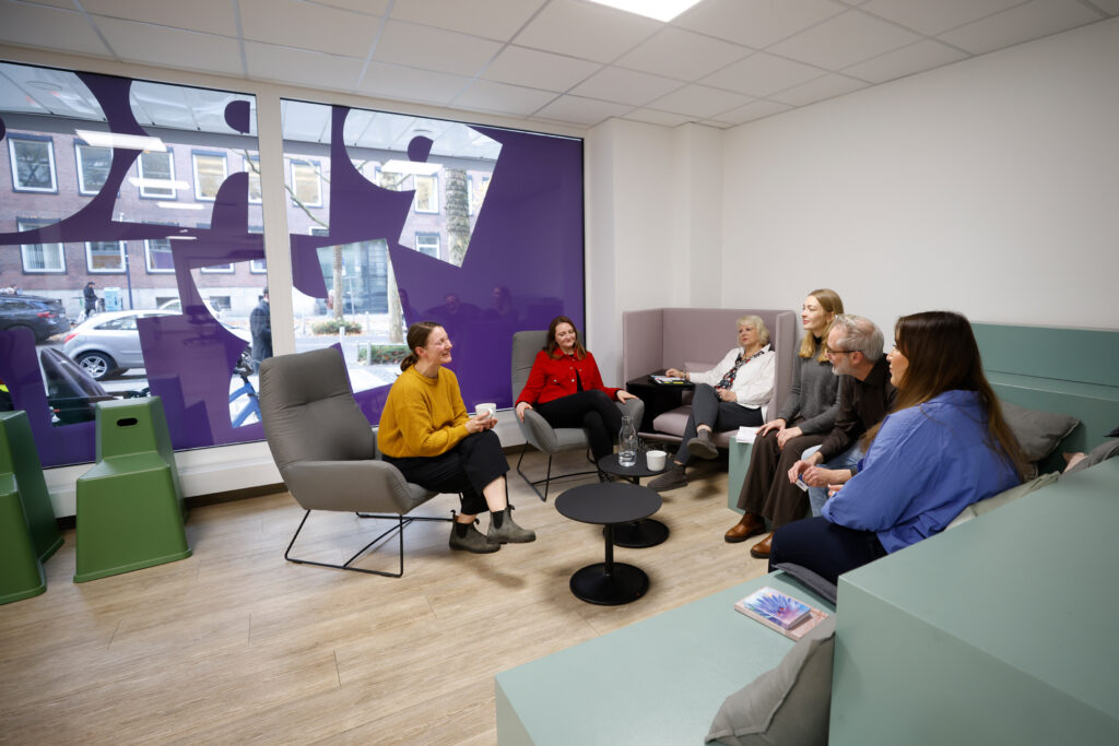Das Bild zeigt die Sitzecke im Projektor. Sechs Personen sitzen dort gemeinsam und unterhalten sich.